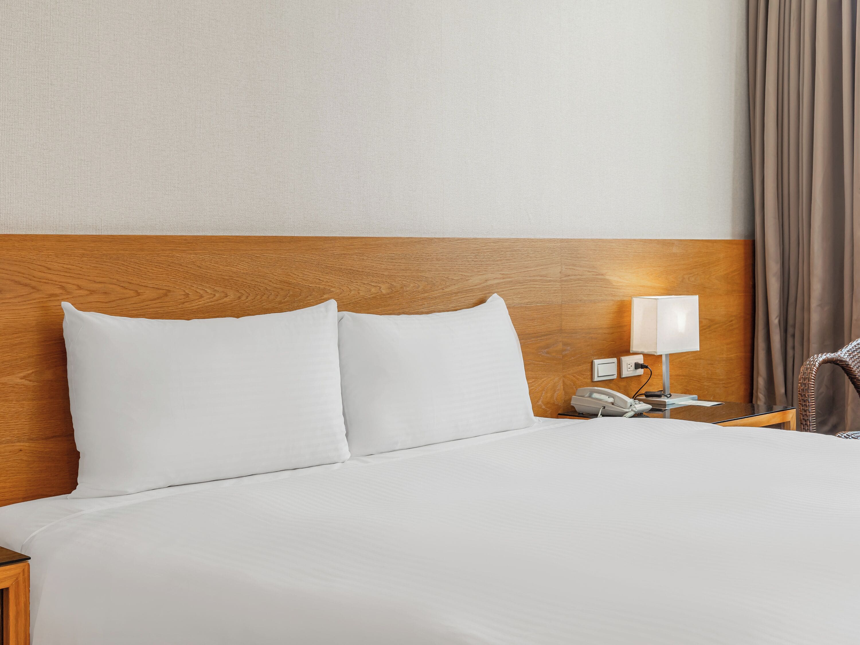 Une chambre d’hôtel avec une tête de lit en bois, du linge de lit blanc, une table de chevet avec une lampe, un téléphone et une chaise.