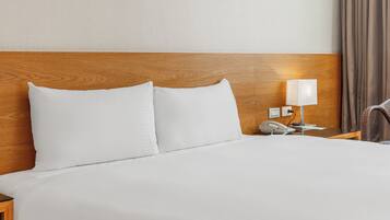 Une chambre d’hôtel avec une tête de lit en bois, du linge de lit blanc, une table de chevet avec une lampe, un téléphone et une chaise.