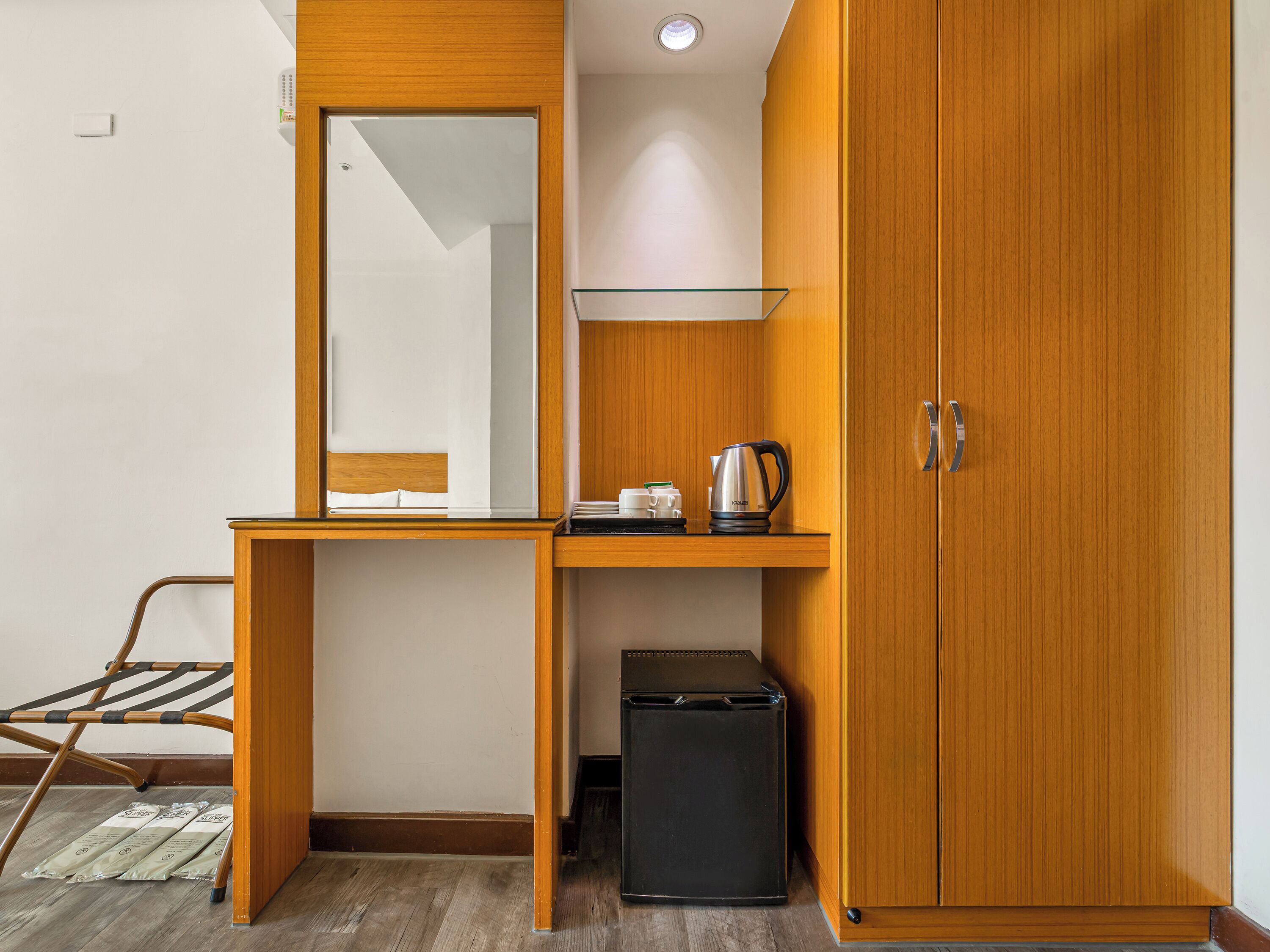 A small room with a wooden desk, a mirror, a shelf, a cabinet, and a black trash bin.