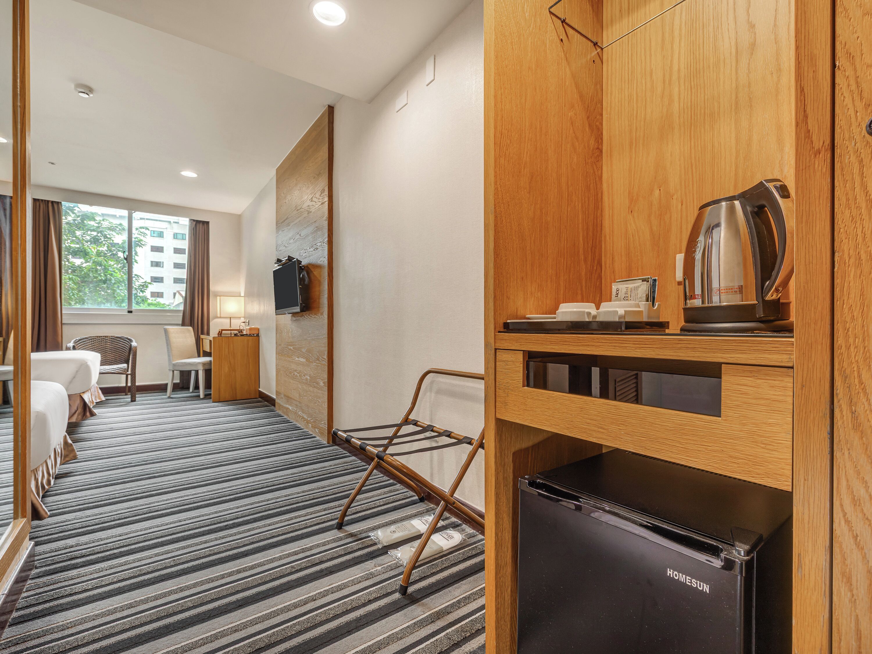 Habitación de hotel con cama, escritorio, silla, televisor, cafetera y refrigerador.