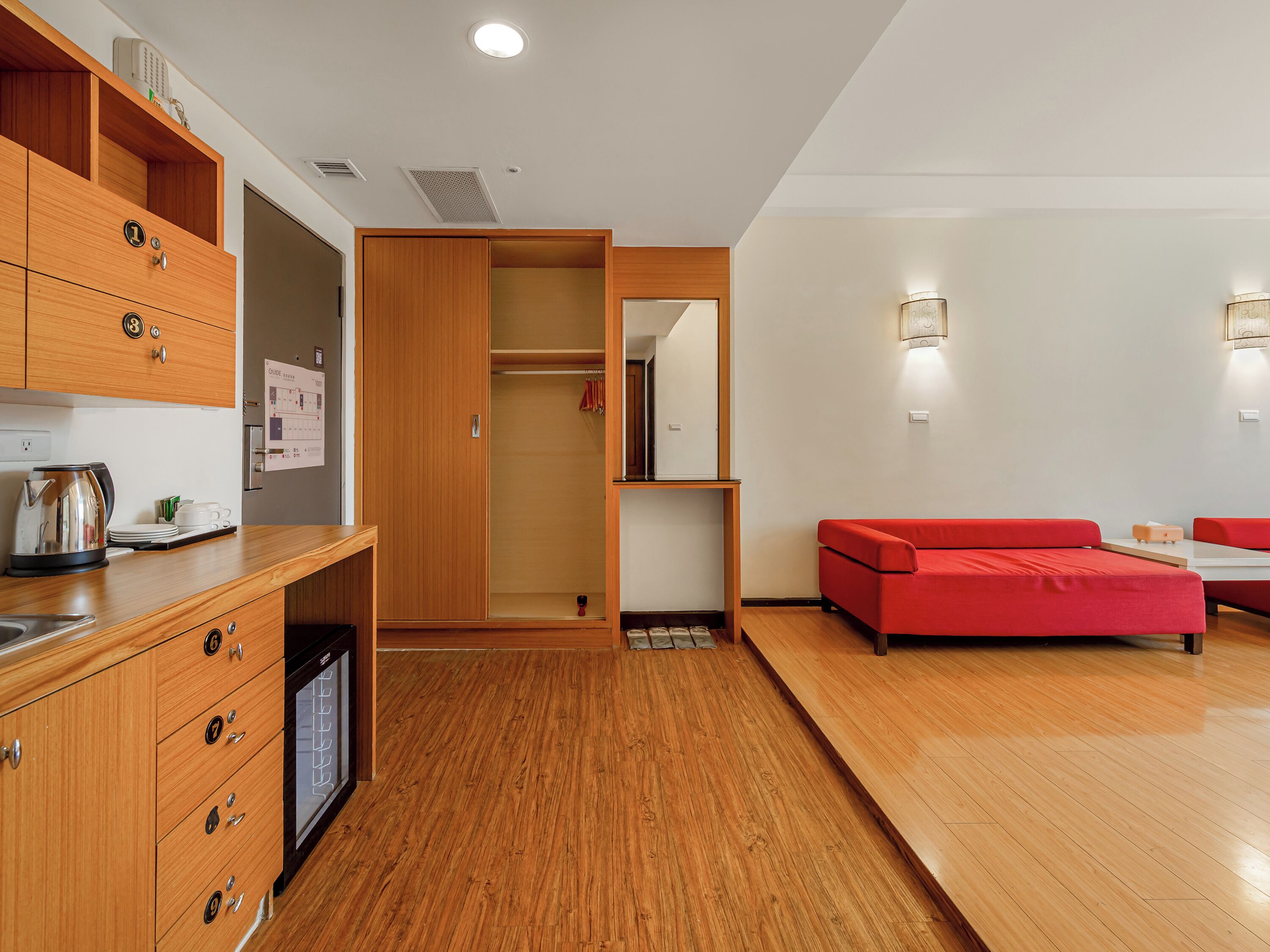 A modern kitchen with wooden cabinets and a built-in dishwasher, a red sofa, and a dining area with a table and chairs.