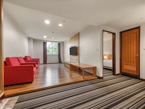 A hotel room with a wooden floor, a TV mounted on the wall, a bed, a desk, and a seating area with red chairs. - Guide Education Culture Hotel Kaohsiung Museum of Fine Arts (Kaohsiung)