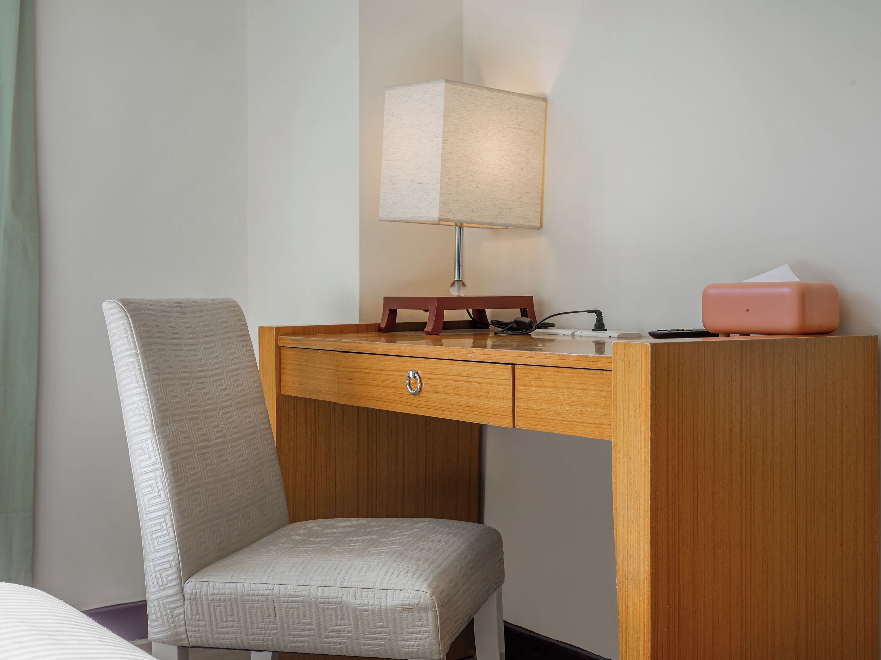 A wooden desk with a lamp, a tissue box, and a chair in a hotel room.