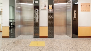 Duas portas de elevador com uma placa de número 7, um aviso de proibido fumar e um mapa turístico na parede.