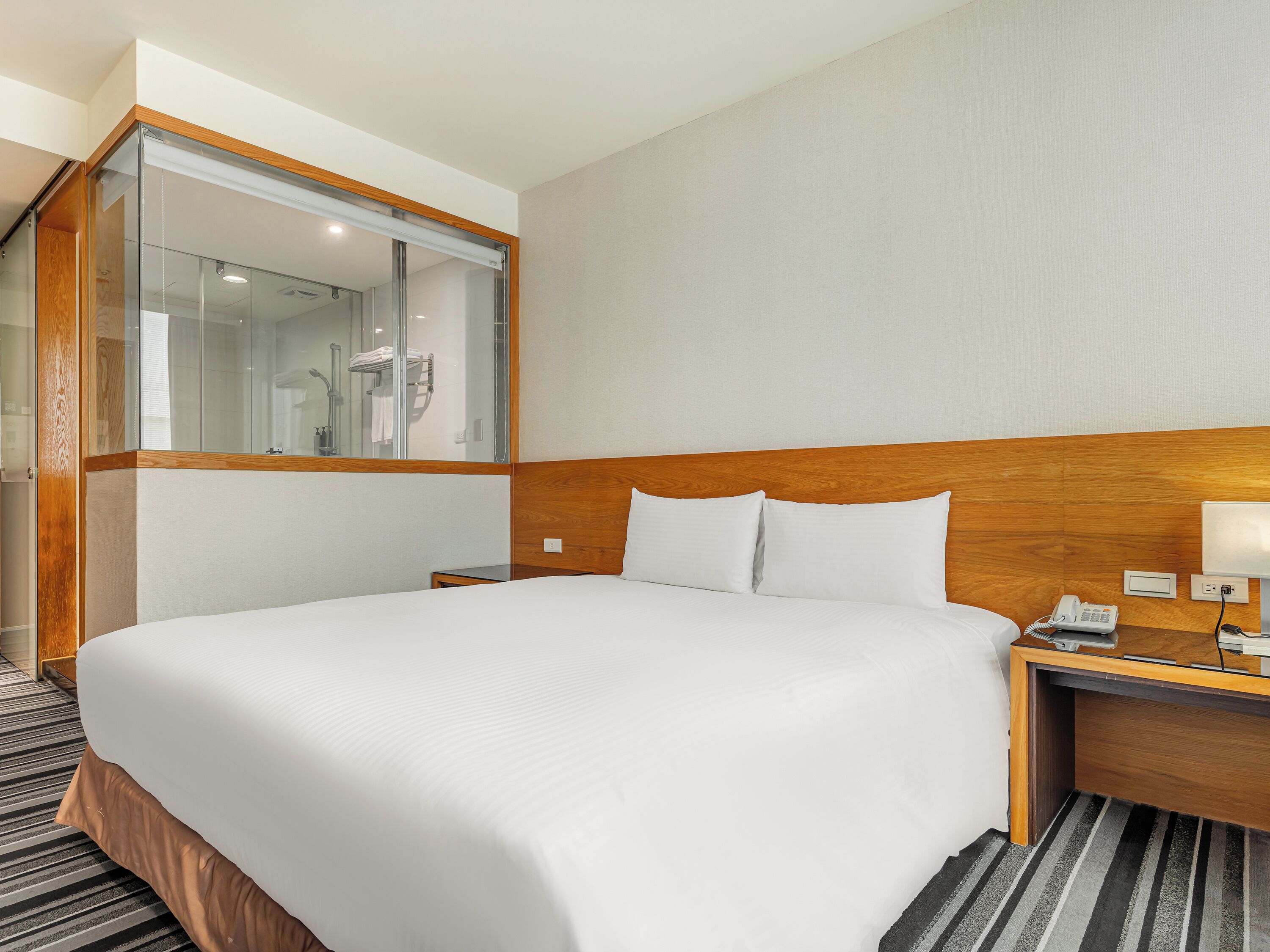A hotel room with a large bed, a wooden headboard, a nightstand with a phone, and a mirror.