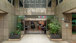Entrada de hotel com uma placa indicando 'Guide-Education Culture Hotel' e o 'Museu de Belas Artes de Kaohsiung' ao fundo.