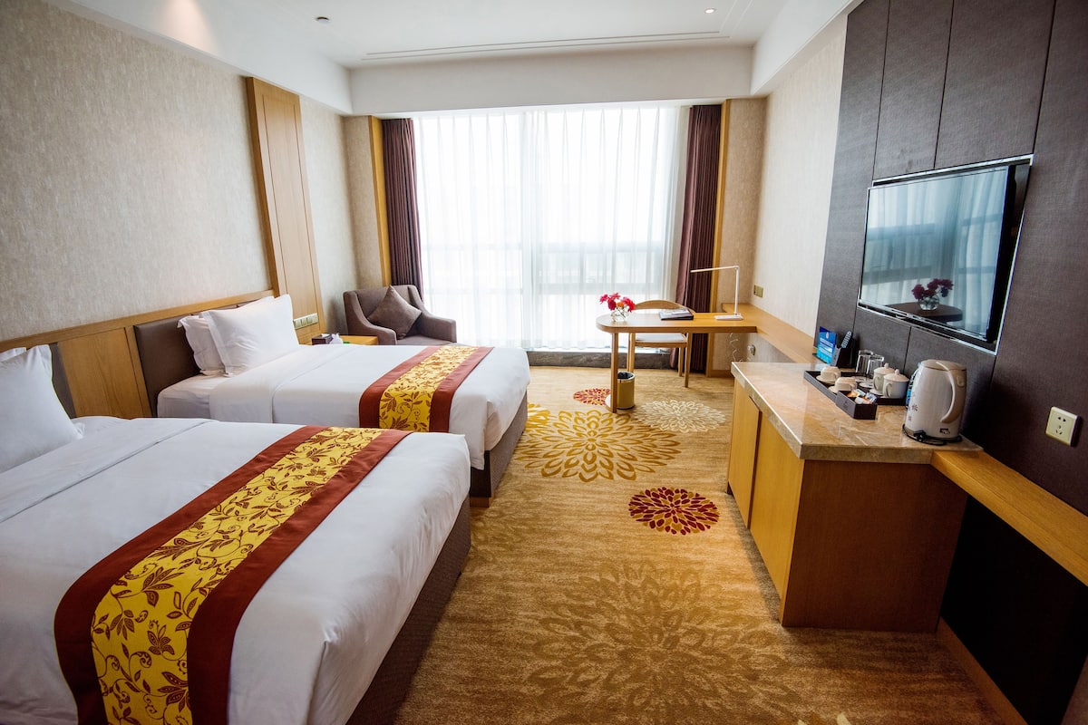 Ein Hotelzimmer mit zwei Betten, einem Schreibtisch, einem Fernseher und Blick auf die Stadt.