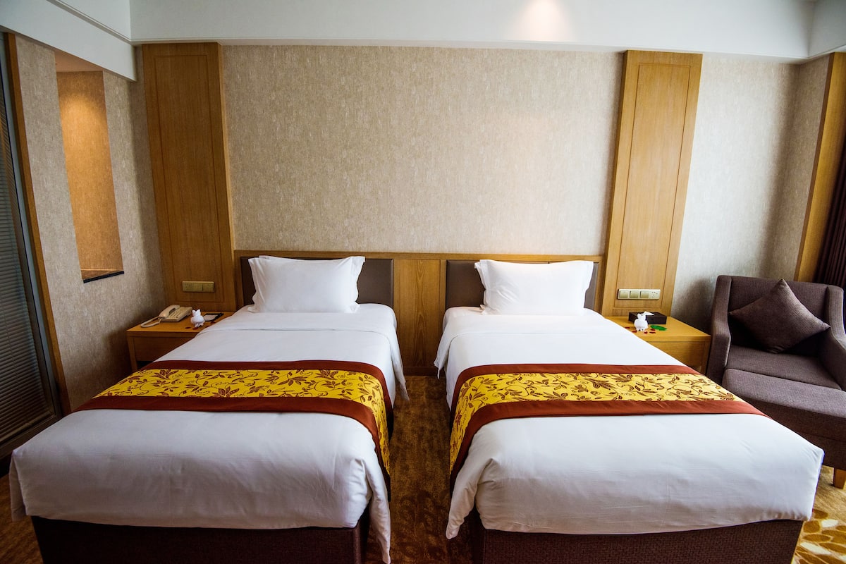 Ein Hotelzimmer mit zwei Betten, einem Holz-Kopfteil, einem braunen Teppich und einem braunen Sessel.