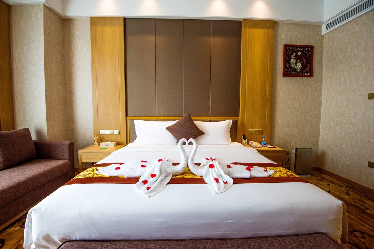 Ein Hotelzimmer mit einem großen Bett, einem braunen Sofa, einem Nachttisch mit Lampe und einer Wanduhr.