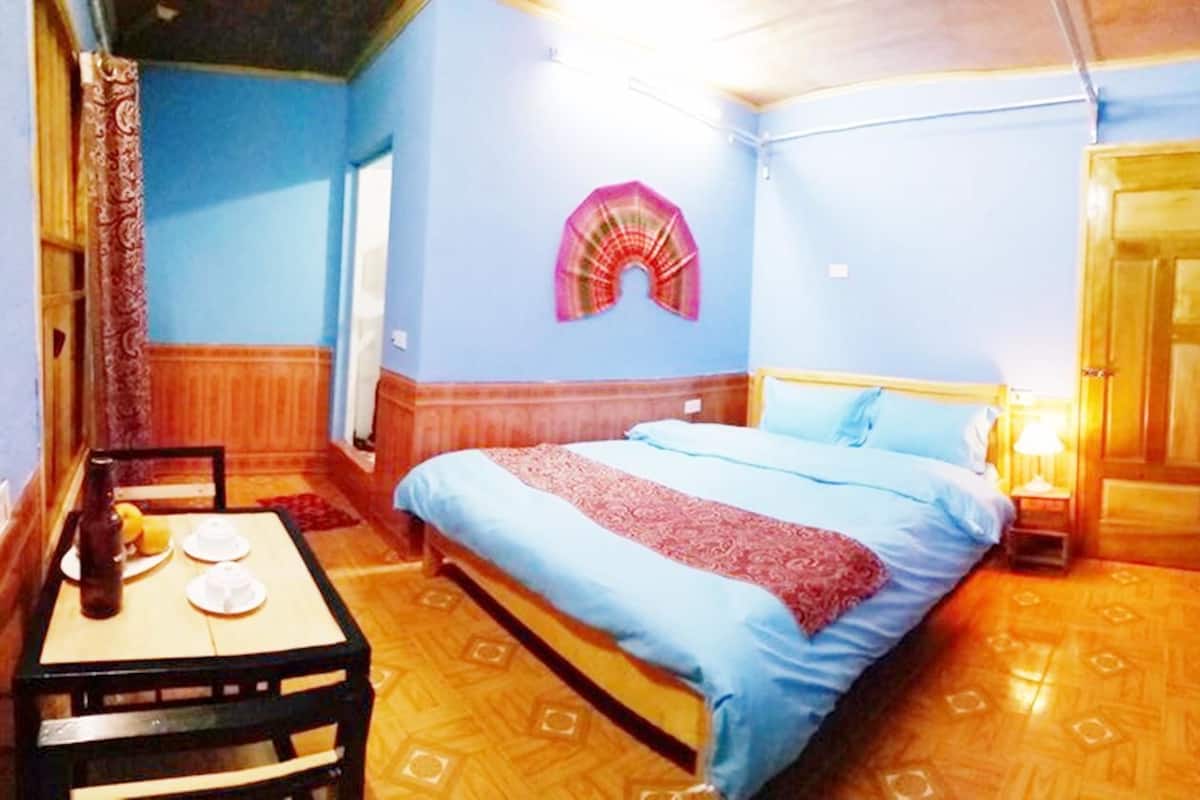 A room with a bed, a table with a bottle and glasses, a wall hanging, and a door.