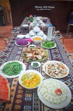 A table with various dishes and a patterned tablecloth. - H'mong Stilt House (Ta Van)
