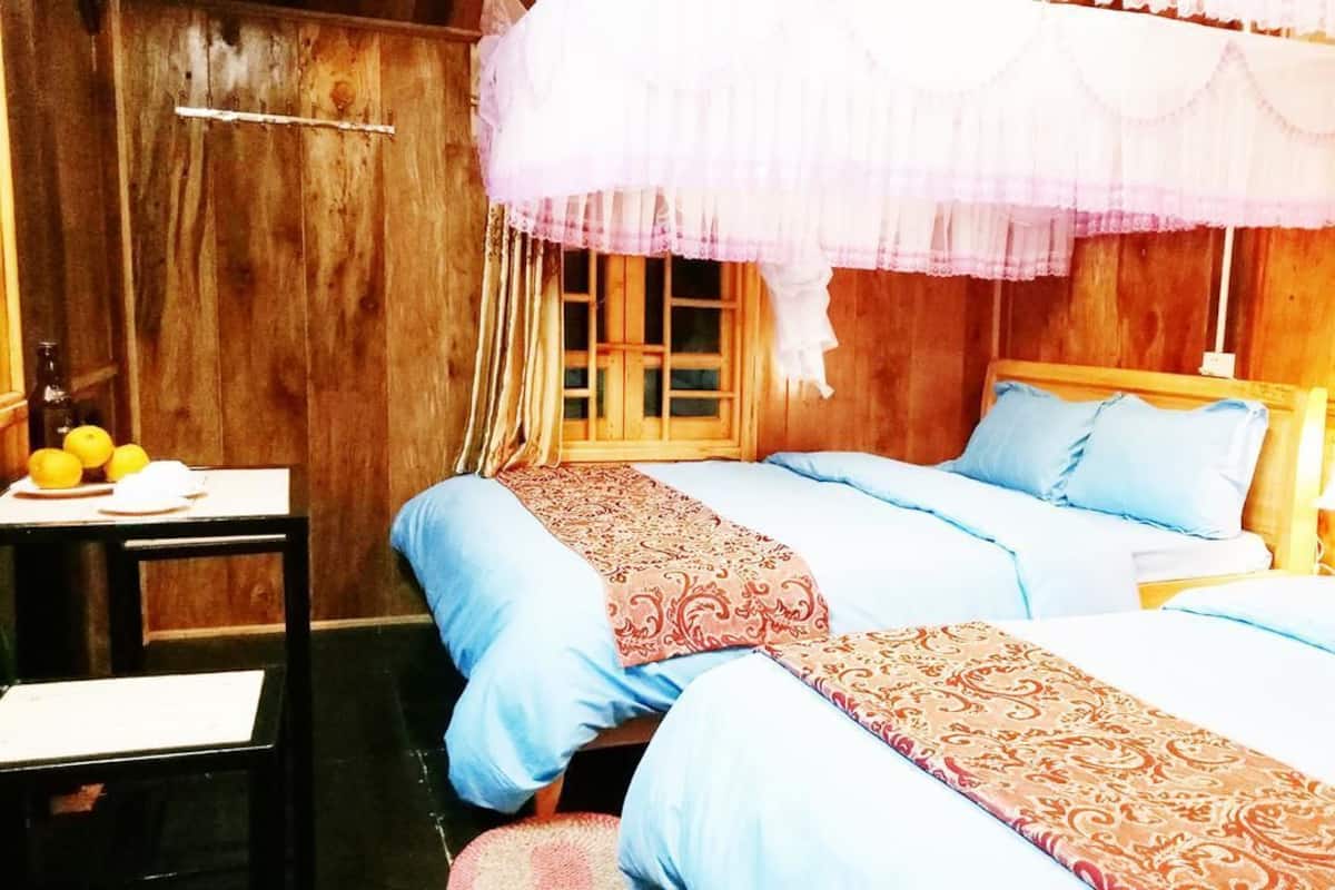 A room with two beds, wooden walls, a window with curtains, and a table with fruits.