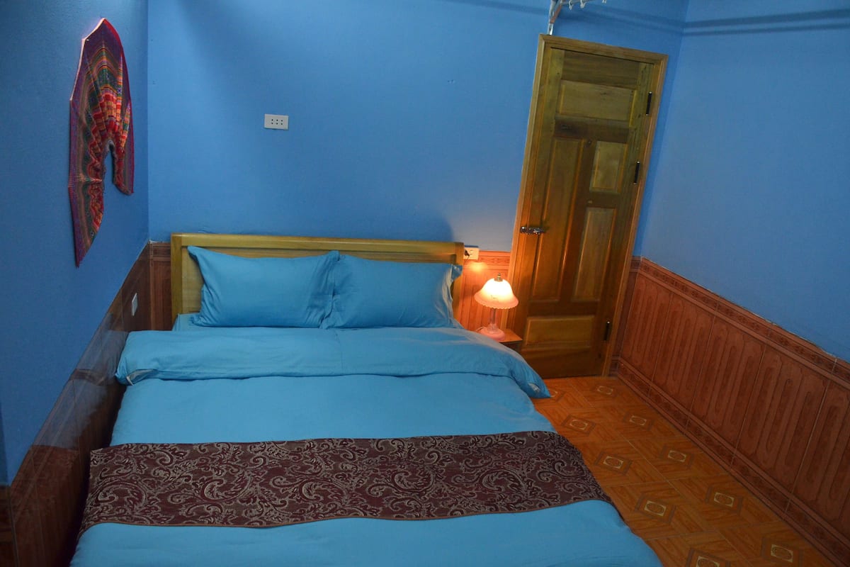A room with a bed, a wooden headboard, a patterned bedspread, and a door.