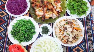 A table with various dishes including purple rice, grilled chicken, green beans, a salad, and sliced watermelon.