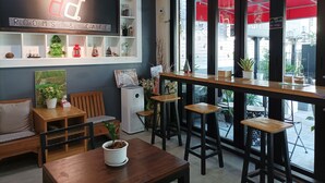 A cozy cafe with a 'Rooms & Cafe' sign, wooden furniture, potted plants, and a view of the street through large windows. - Double D Rooms & Cafe (Bangkok)