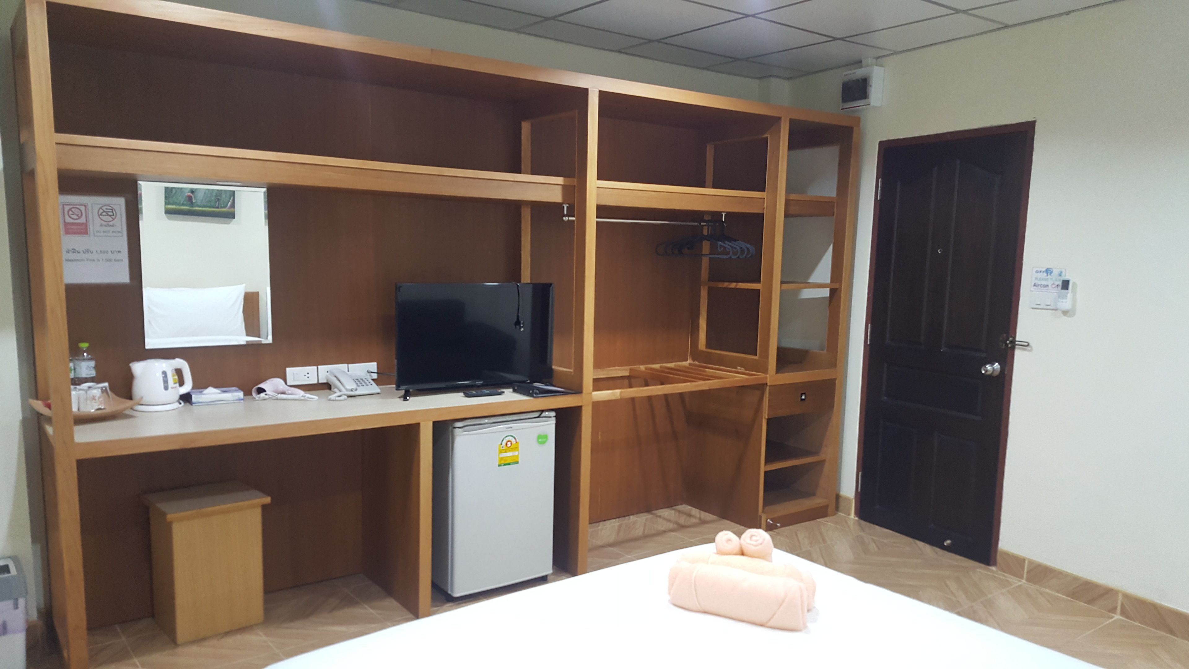 A hotel room with a wooden desk, a television, a small refrigerator, and a bed with pink towels.