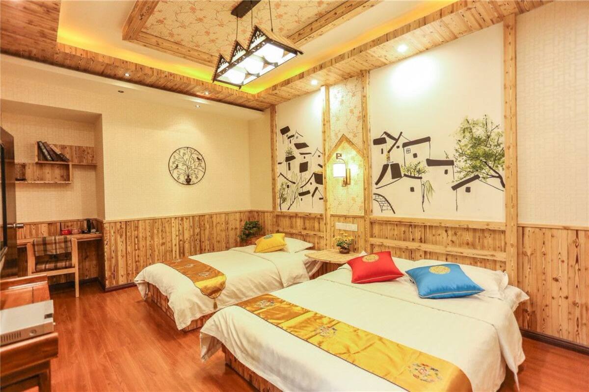 A hotel room with two beds, wooden walls, a small table, and a chair.