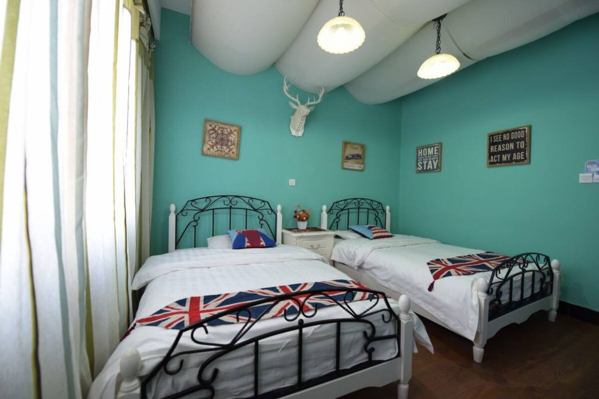A room with two beds, teal walls, a ceiling with a white deer head decoration, and a few wall-mounted signs.