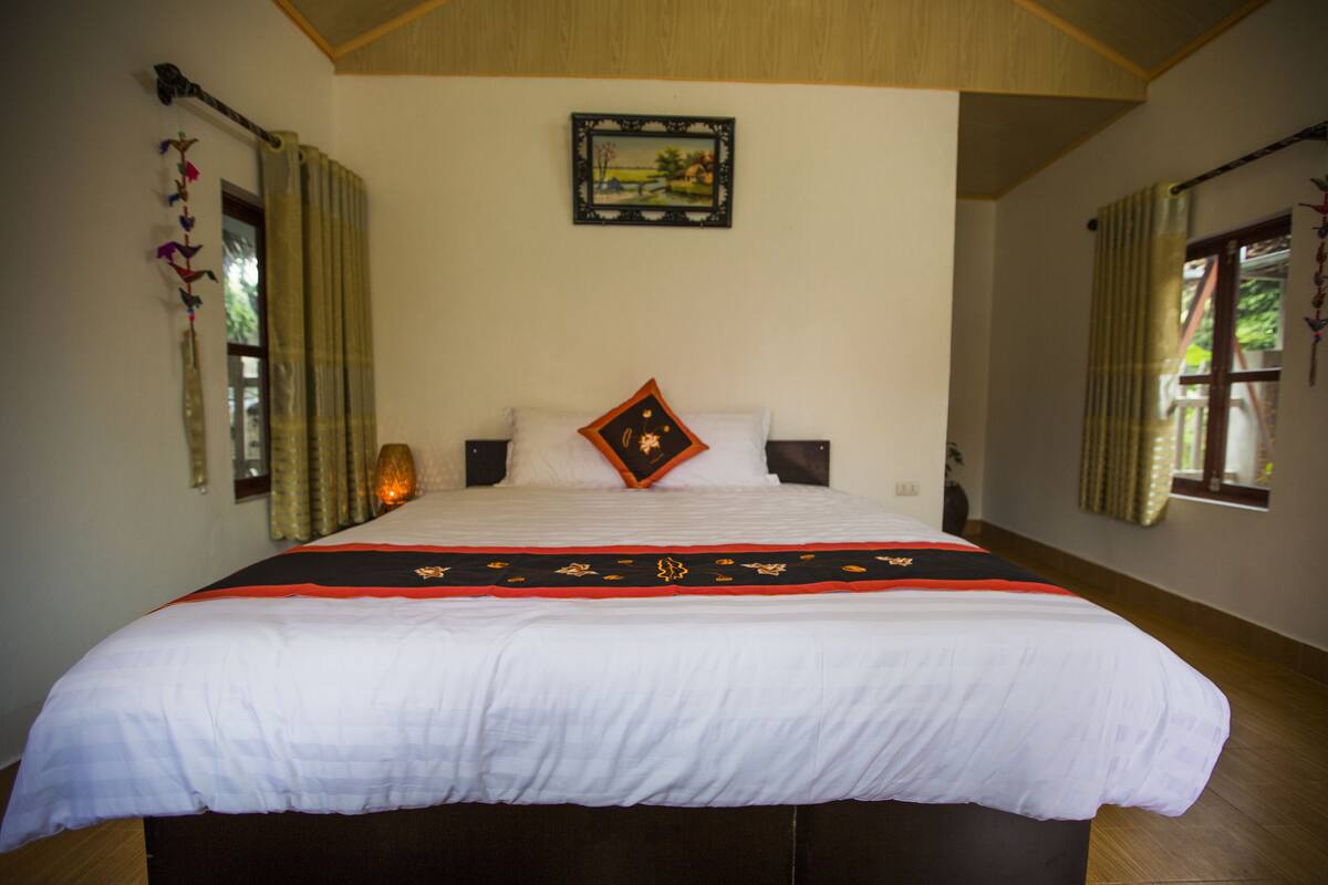A large bed with a white and red bedspread, two pillows, and a framed picture on the wall.