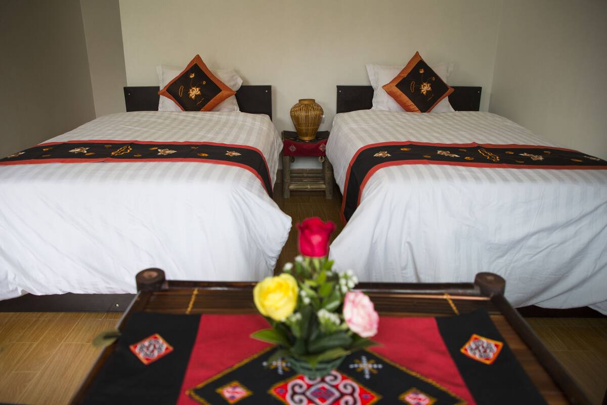 A hotel room with two beds, a small table with a vase of flowers, and a decorative mat.