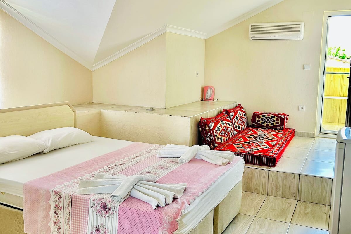 A bedroom with a bed, a sofa, a red patterned rug, and a ceiling fan.