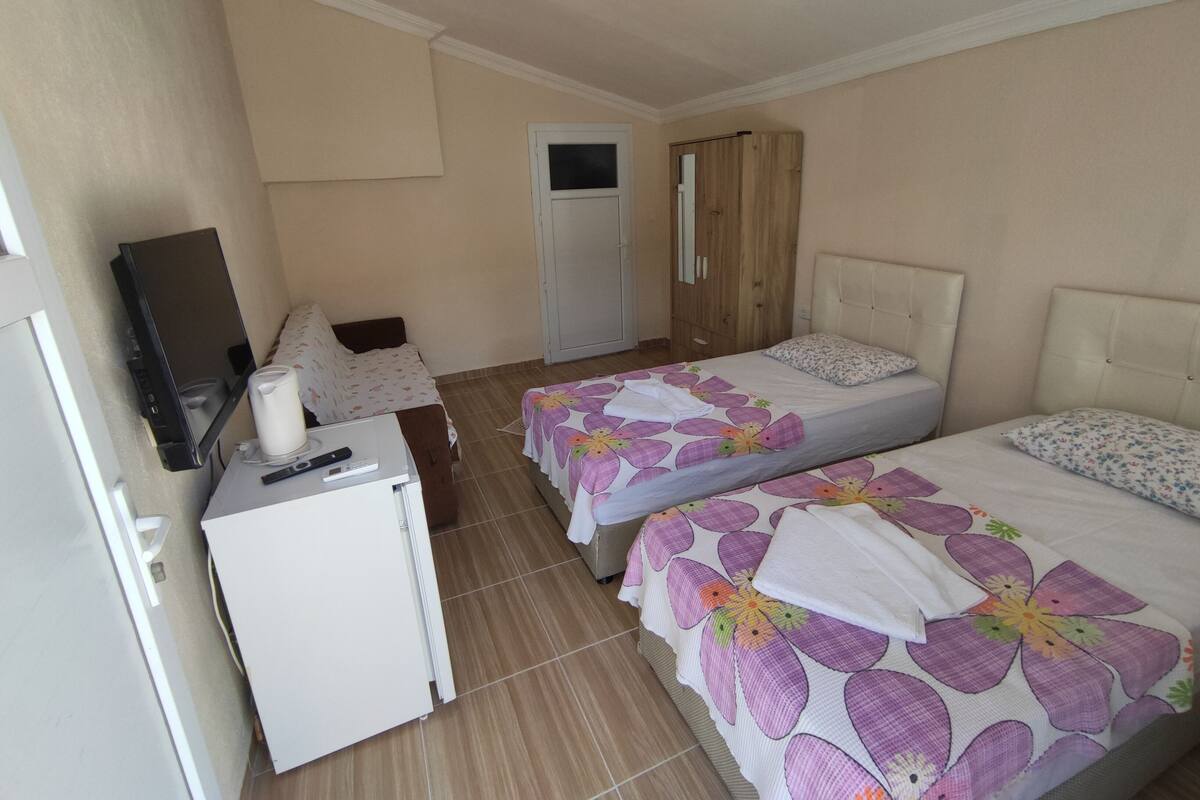 A hotel room with two beds, a small desk with a television, a refrigerator, and a wardrobe.