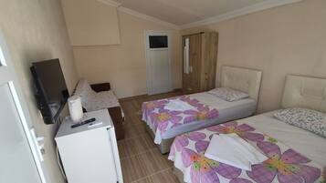 Habitación de hotel con dos camas, un escritorio pequeño con televisor, refrigerador y armario.
