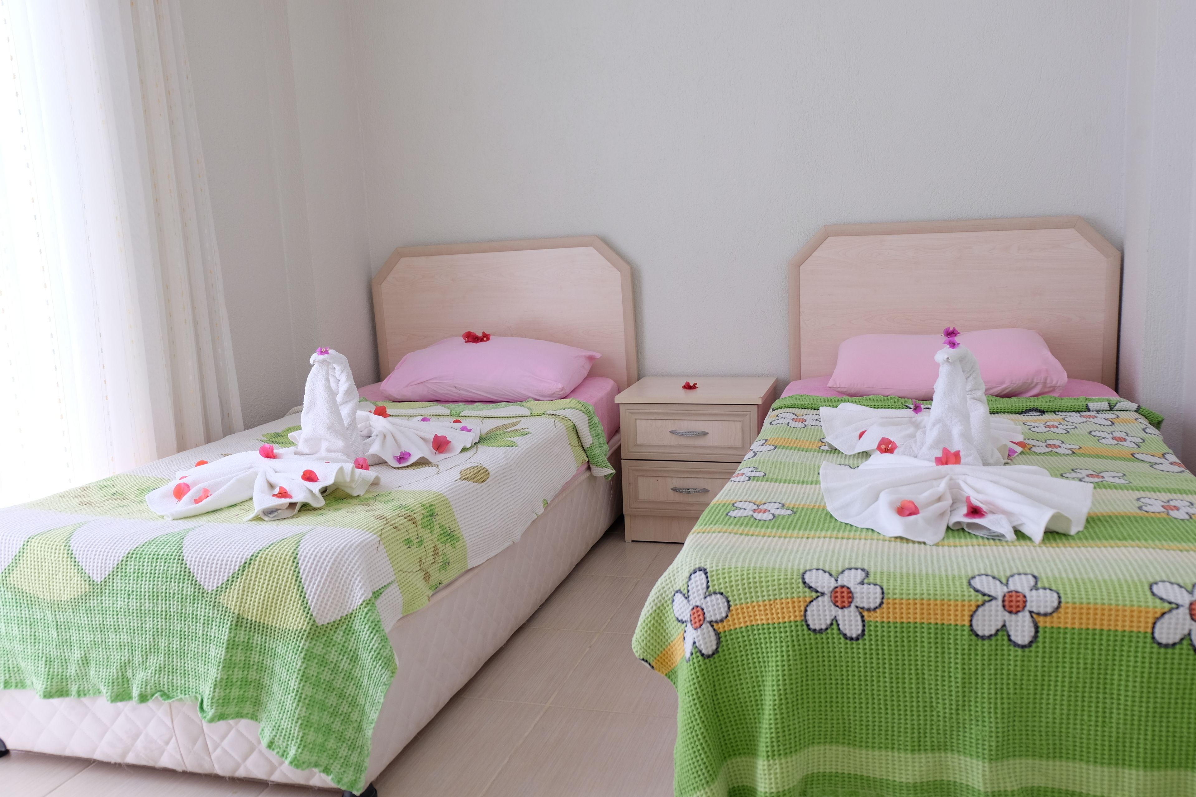Deux lits jumeaux avec des oreillers roses, une tête de lit en bois et une couvre-lit à motifs floraux verts.