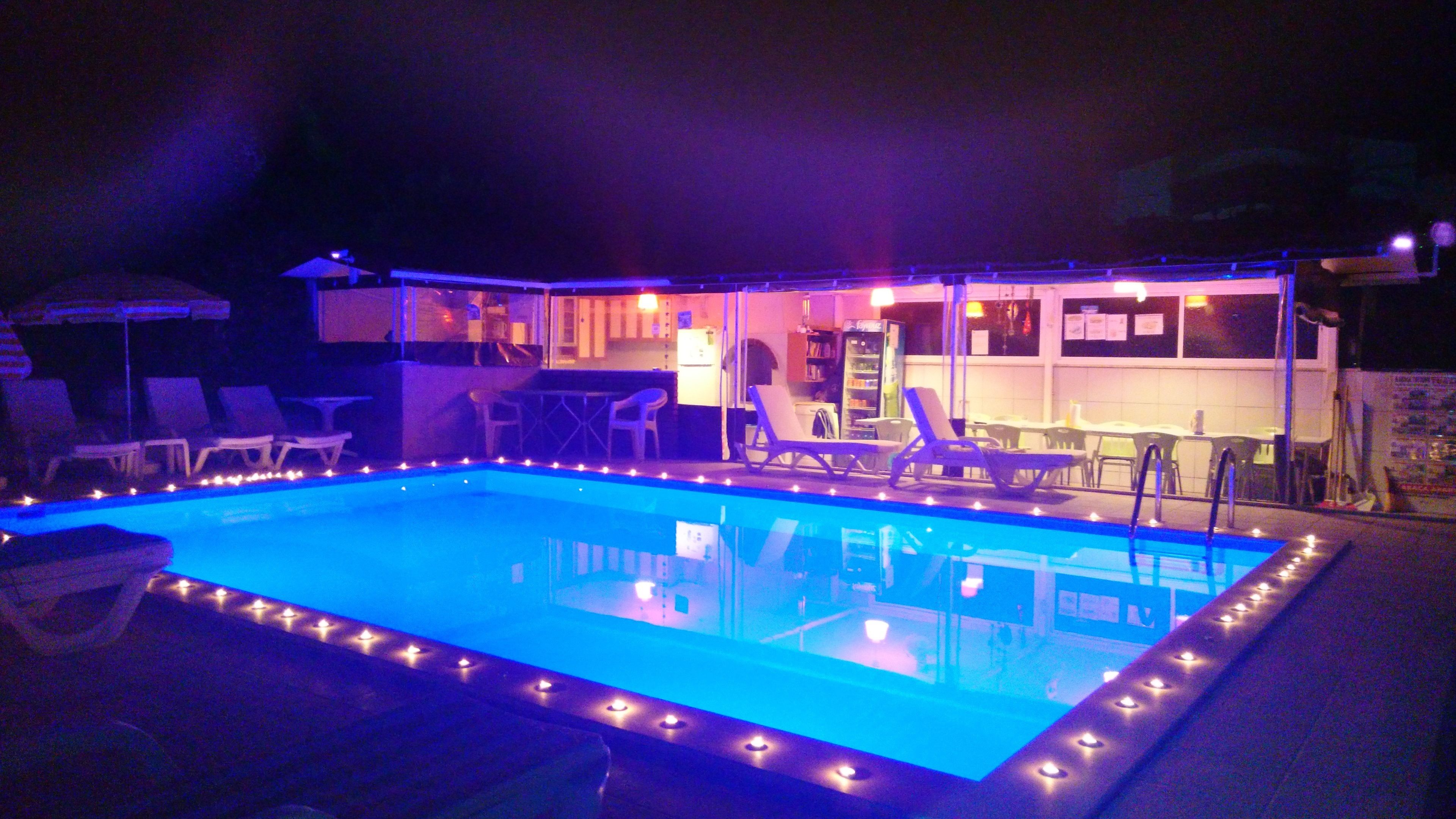 A swimming pool with lights along the edge, surrounded by lounge chairs and a bar area.