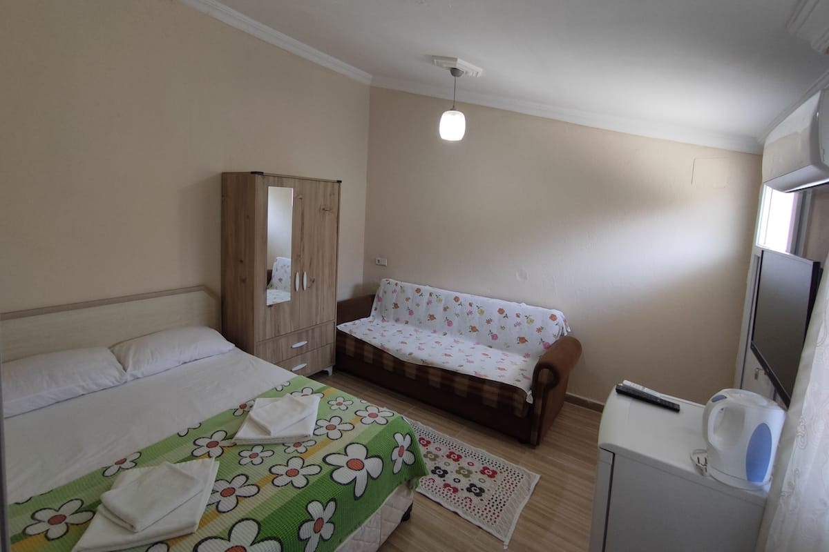 A bedroom with a bed, a wardrobe, a sofa, a coffee machine, and a small table.