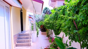 A narrow pathway with steps leading to a door, surrounded by lush greenery and potted plants. - Karaca Apart Hotel (Ortaca)