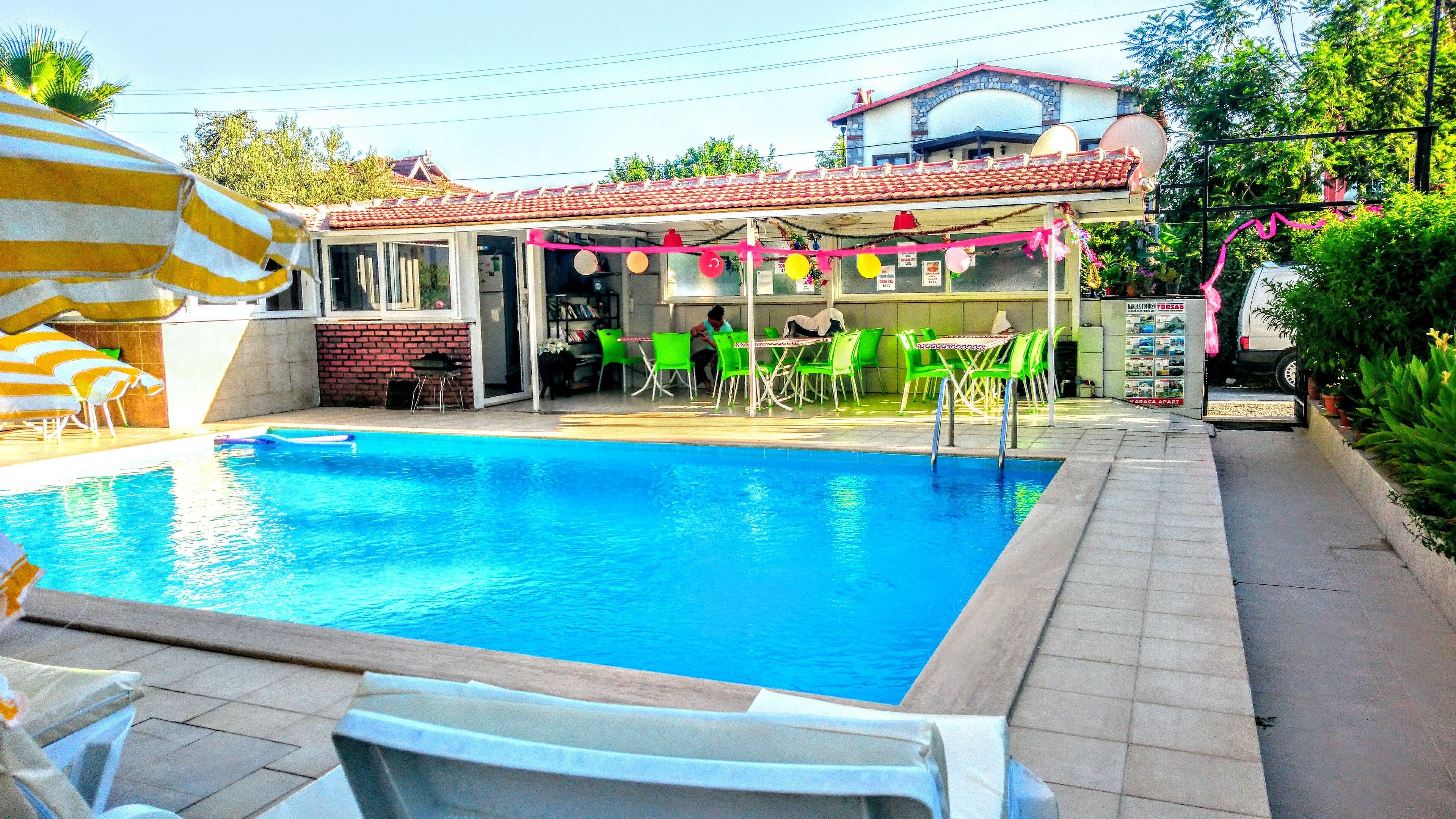 Une piscine avec des chaises vertes et un espace patio couvert.