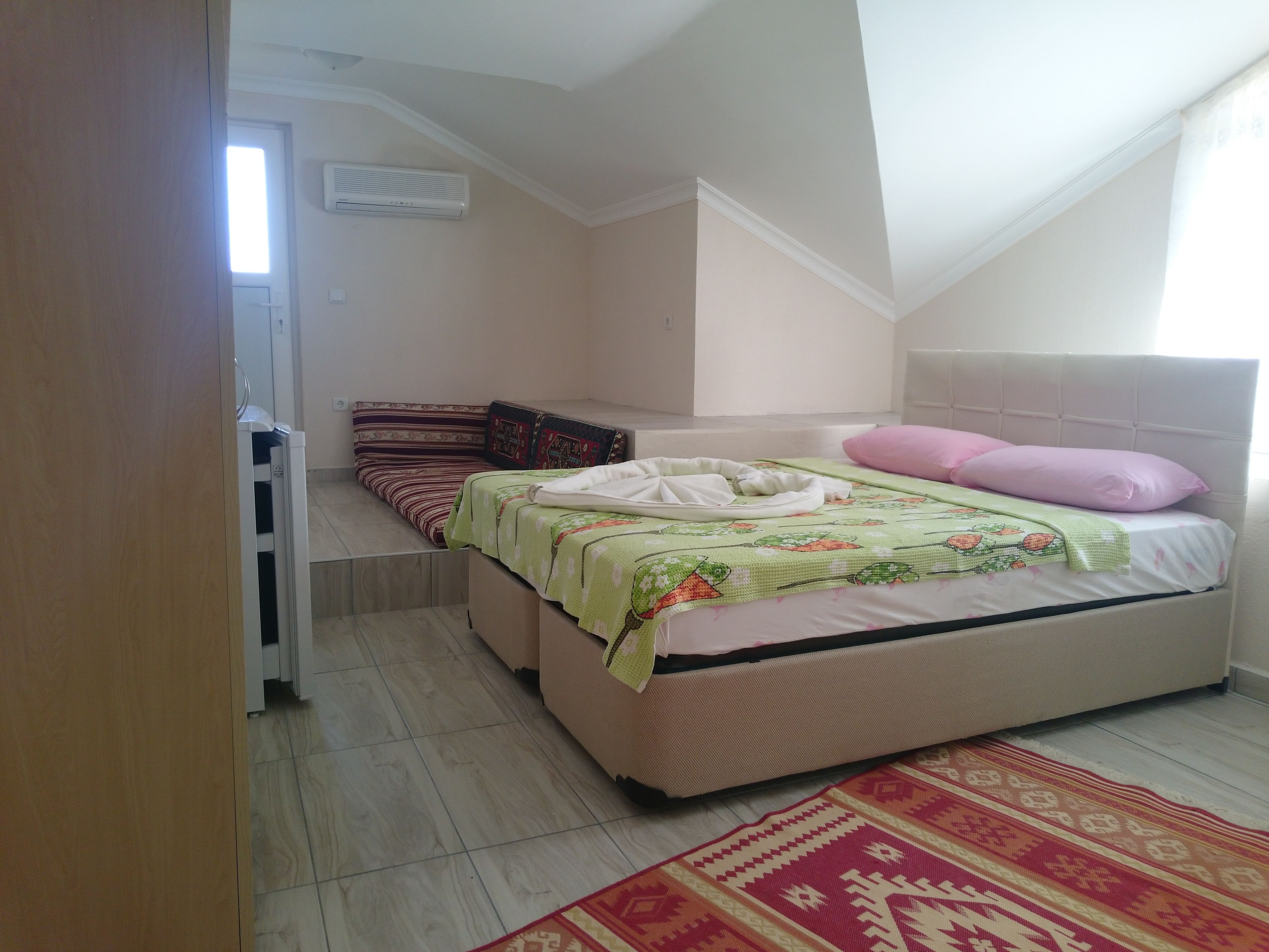 A bedroom with a bed, pillows, a blanket, a rug, and a window.