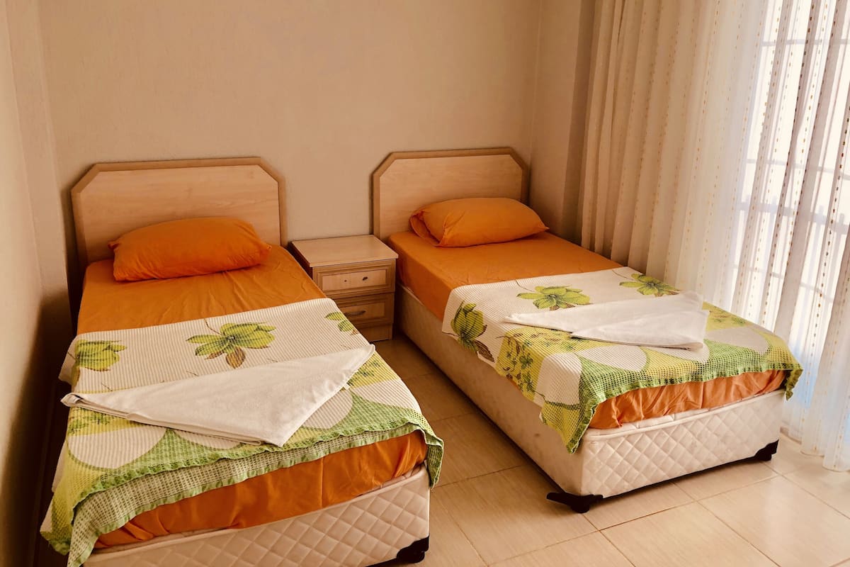 Two single beds with orange bedding and green leaf-patterned blankets, wooden headboards, and a nightstand between them.