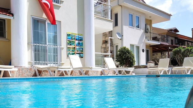A swimming pool with lounge chairs, a flag, and a building with balconies and windows. - Karaca Apart Hotel (Ortaca)