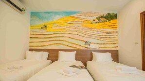 Habitación de hotel con tres camas, un cuadro grande de campos escalonados y un equipo de aire acondicionado en la pared.