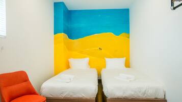 Une chambre avec deux lits, un fauteuil orange et un mur orné d’une fresque bleue et jaune.