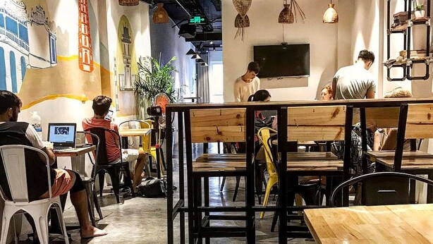 Un restaurante con mesas y sillas de madera, un televisor montado en la pared y personas cenando.