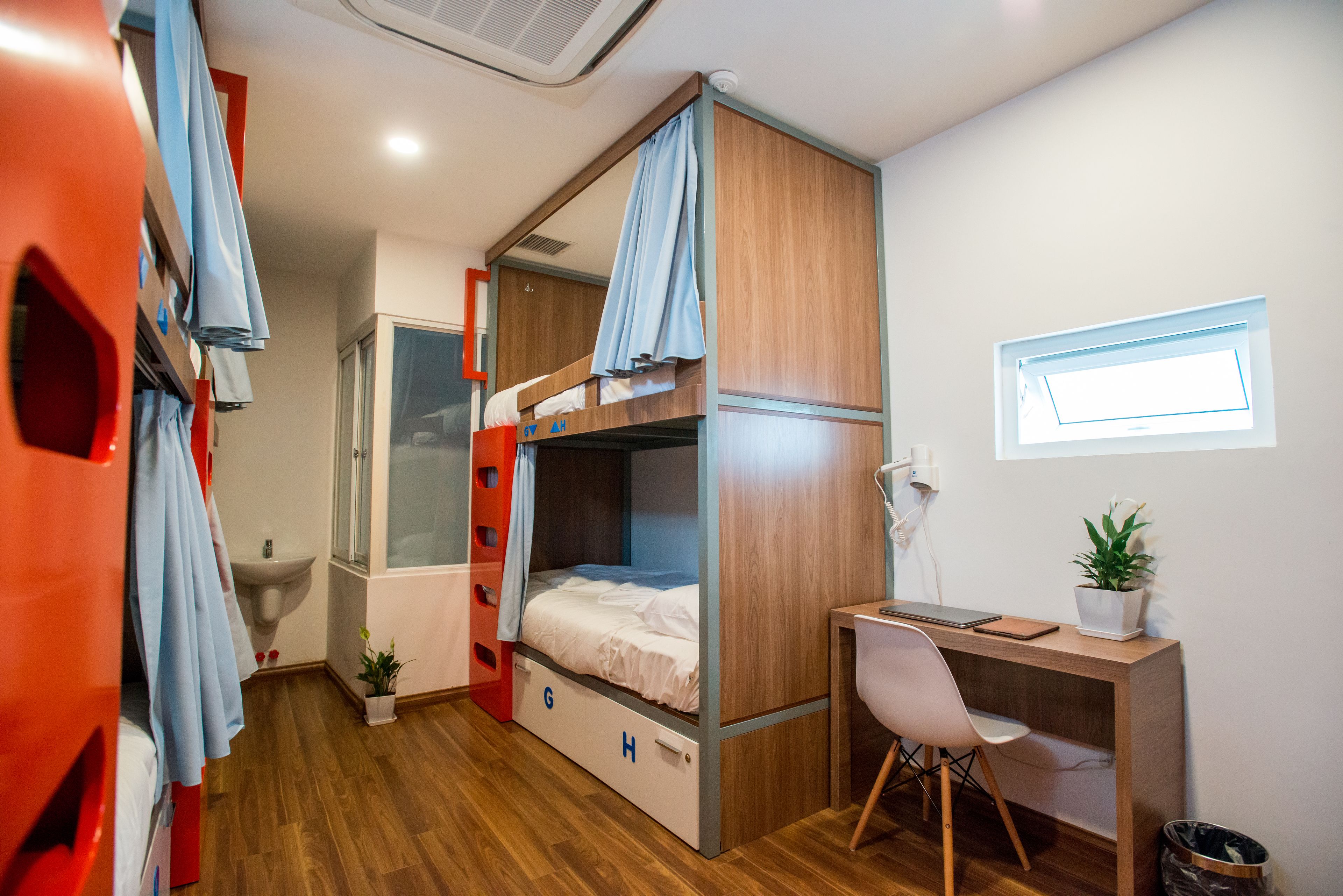 A compact room with bunk beds, a desk, a chair, a sink, and a window.