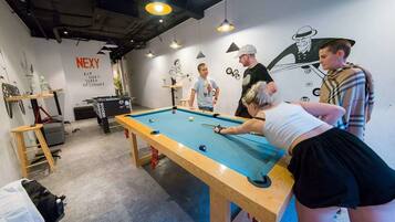 A pool table in a room with a 'NEXY' sign, a wall with a cartoon character, and a person playing pool.