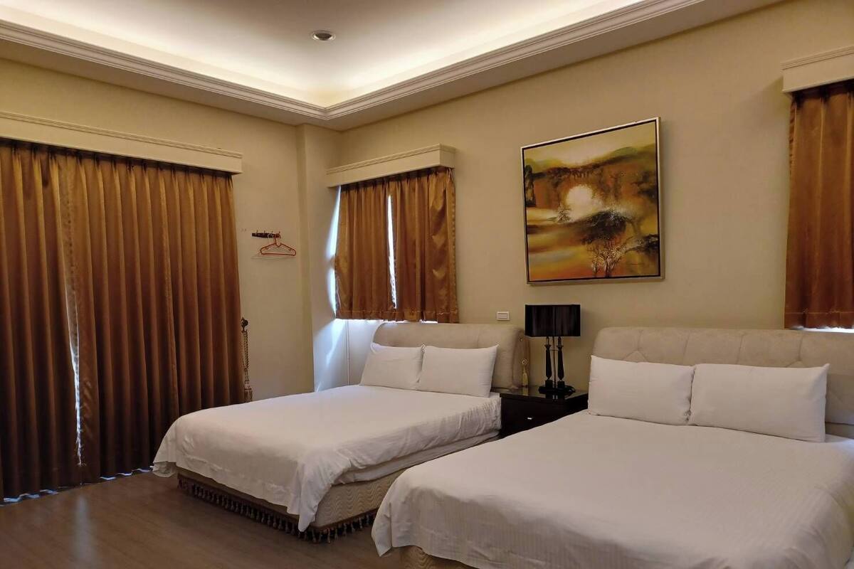 A hotel room with two beds, a painting on the wall, and a lamp on a bedside table.