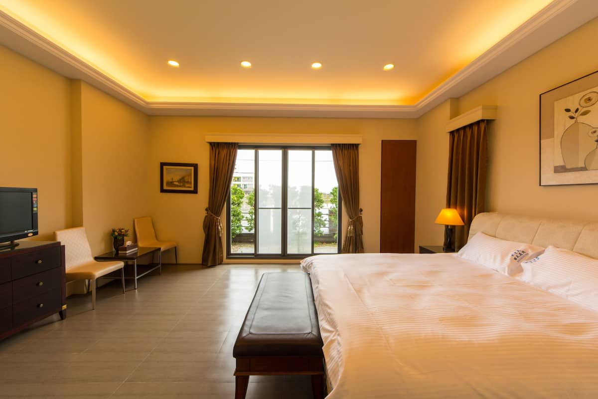 A hotel room with a large bed, a desk with a chair, a television, and a window with curtains.