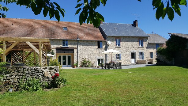 A stone house with a tiled roof, a covered patio, and a stone wall with flowers. - Gîtes de Campagne (Fursac)