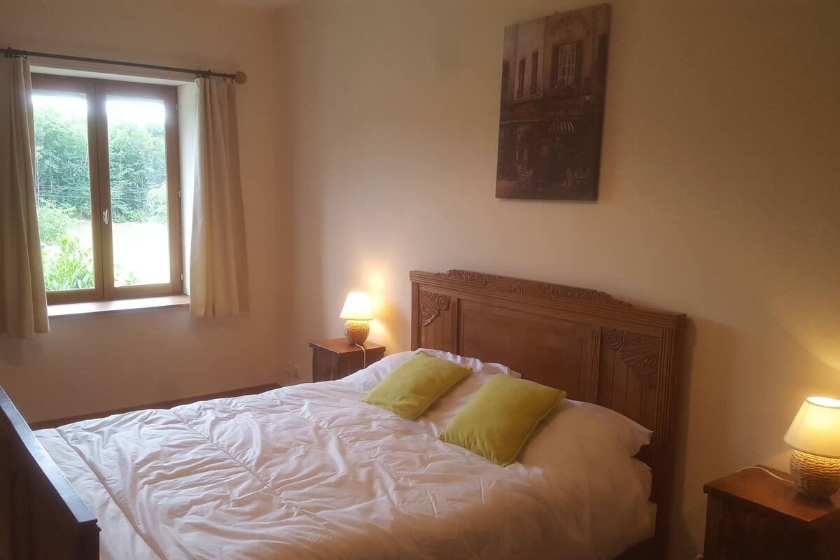 A bedroom with a bed, two bedside lamps, a window with curtains, and a wall-mounted painting.
