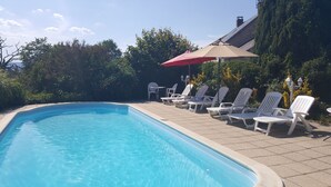 A swimming pool with white lounge chairs and a red umbrella. - Gîtes de Campagne (Fursac)