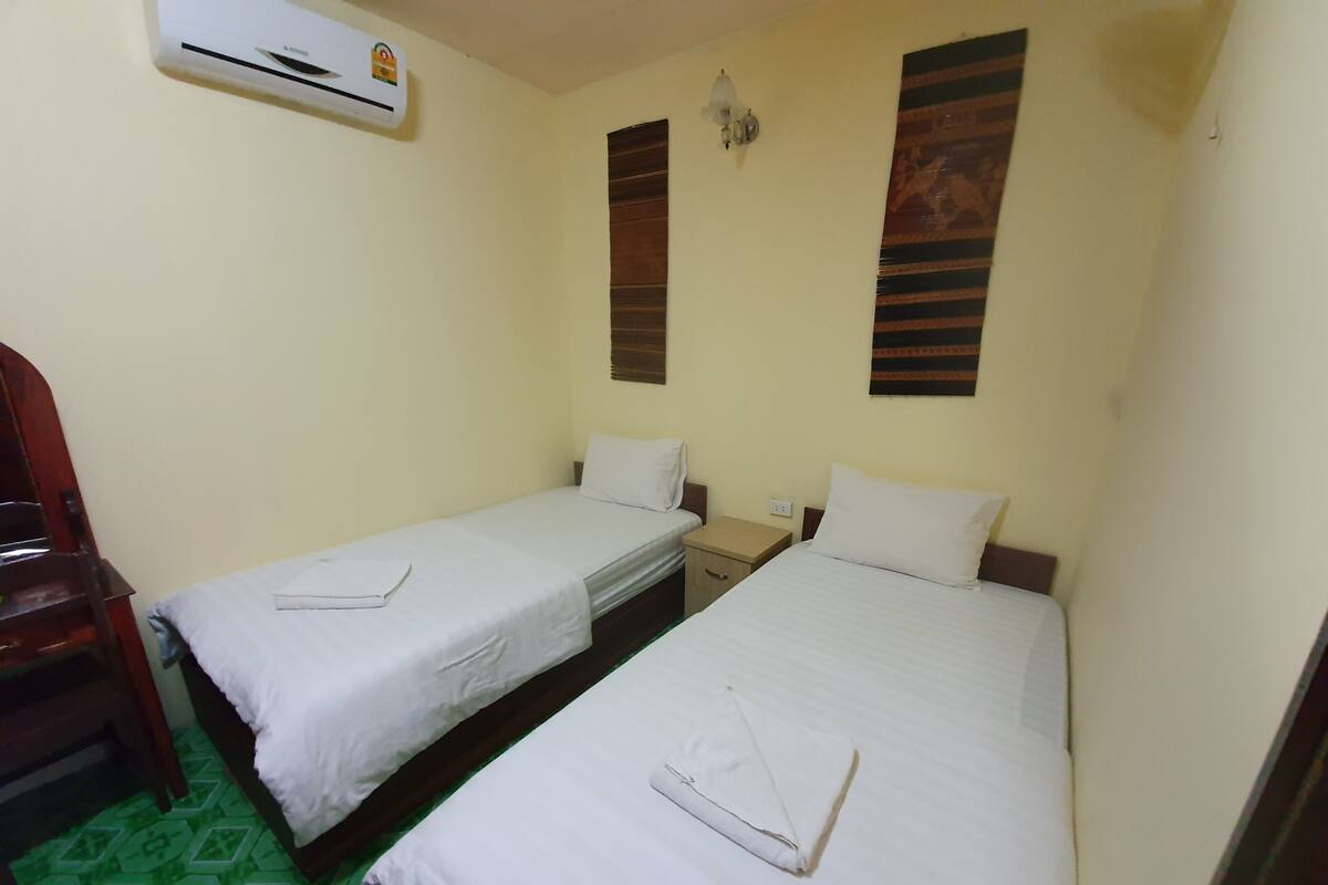 Een kamer met twee eenpersoonsbedden, een houten stoel, een klein tafeltje en een airconditioning.