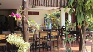 Un espace extérieur aménagé avec des bancs et des tables en bois, entouré de plantes en pot et de fleurs suspendues.