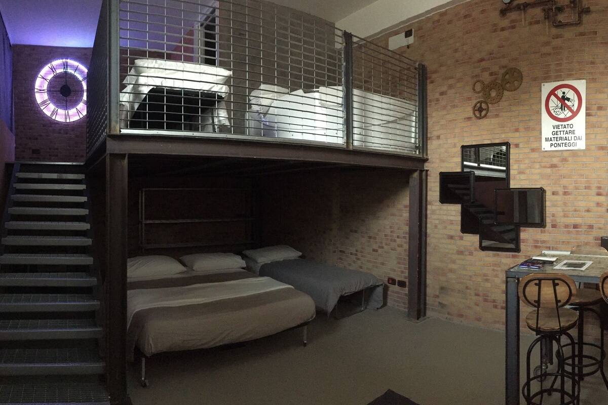 A dormitory room with bunk beds, a staircase, a desk with two chairs, and a no-smoking sign.