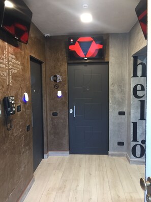 A hallway with a black door, a wall-mounted Wi-Fi sign, a phone, and a 'hello' sign. - B2in Suite & Office (Capriate San Gervasio)