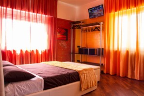A hotel room with a bed, a TV mounted on the wall, and a wardrobe with hanging clothes. - B2in Suite & Office (Capriate San Gervasio)